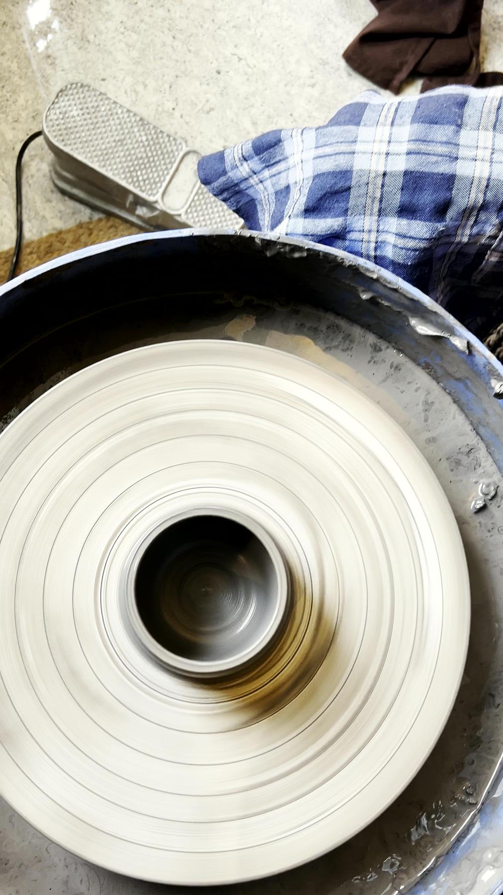 Looking down at two hands steadying a cylinder rising on the wheel