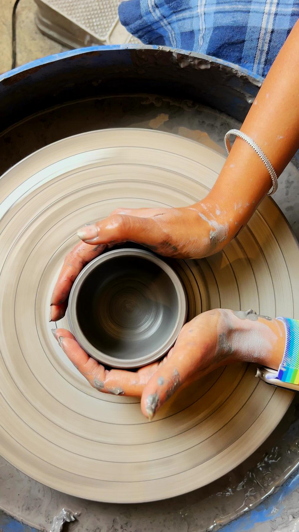 A part-thrown cylinder on the wheel, walls still uneven, hands resting on the rim