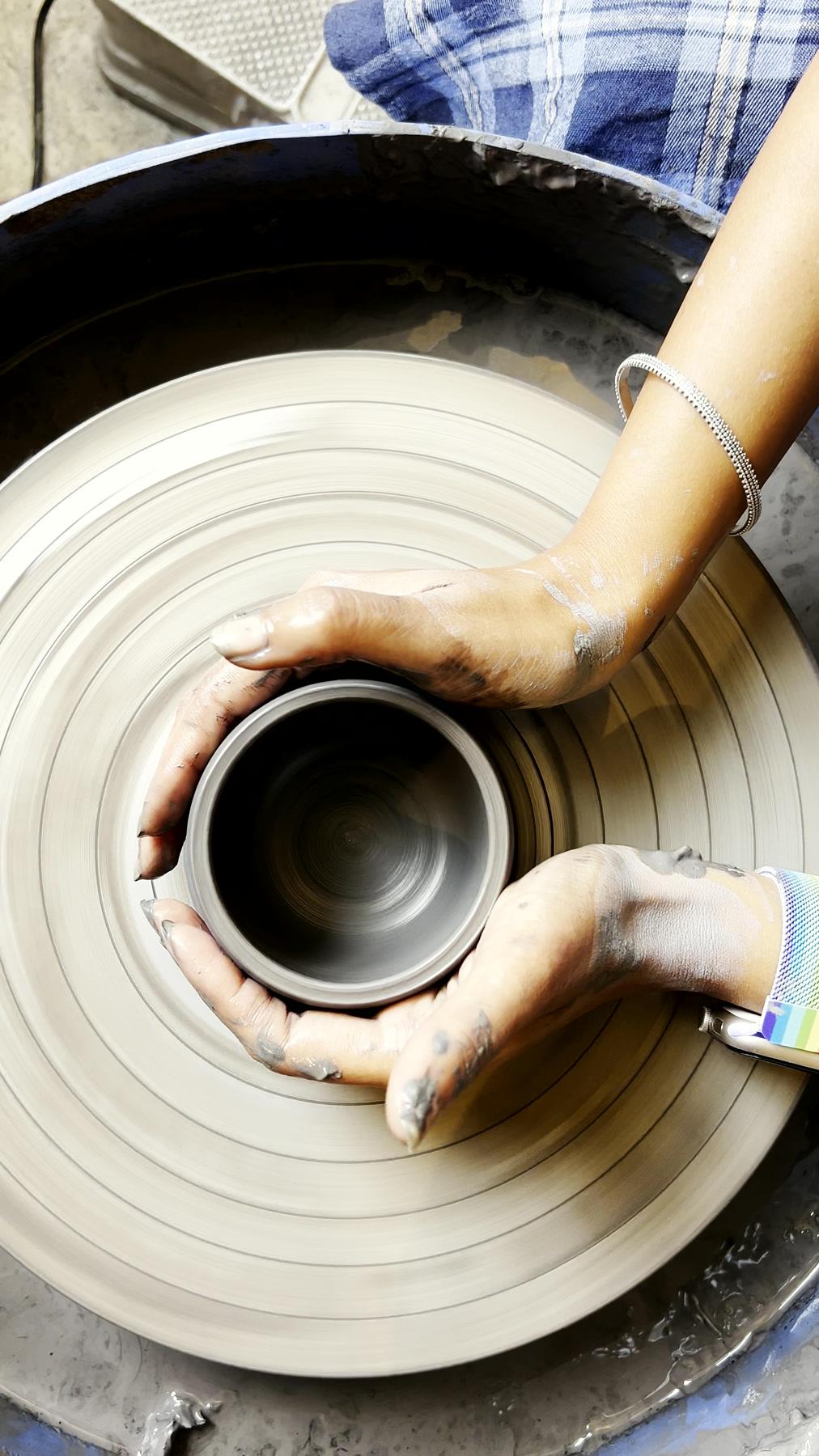 A part-thrown cylinder on the wheel, walls still uneven, hands resting on the rim