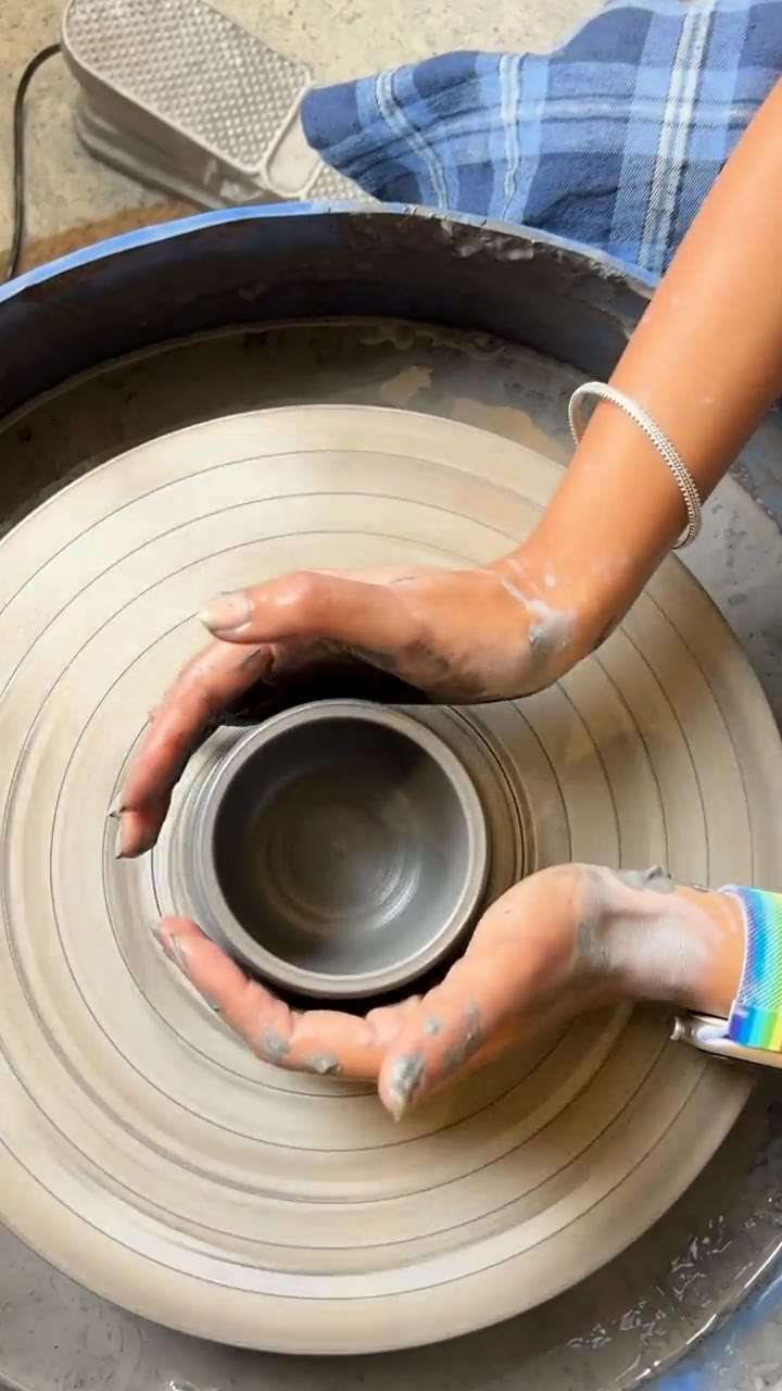 Overhead view of clay-covered hands opening a cylinder on a spinning wheel