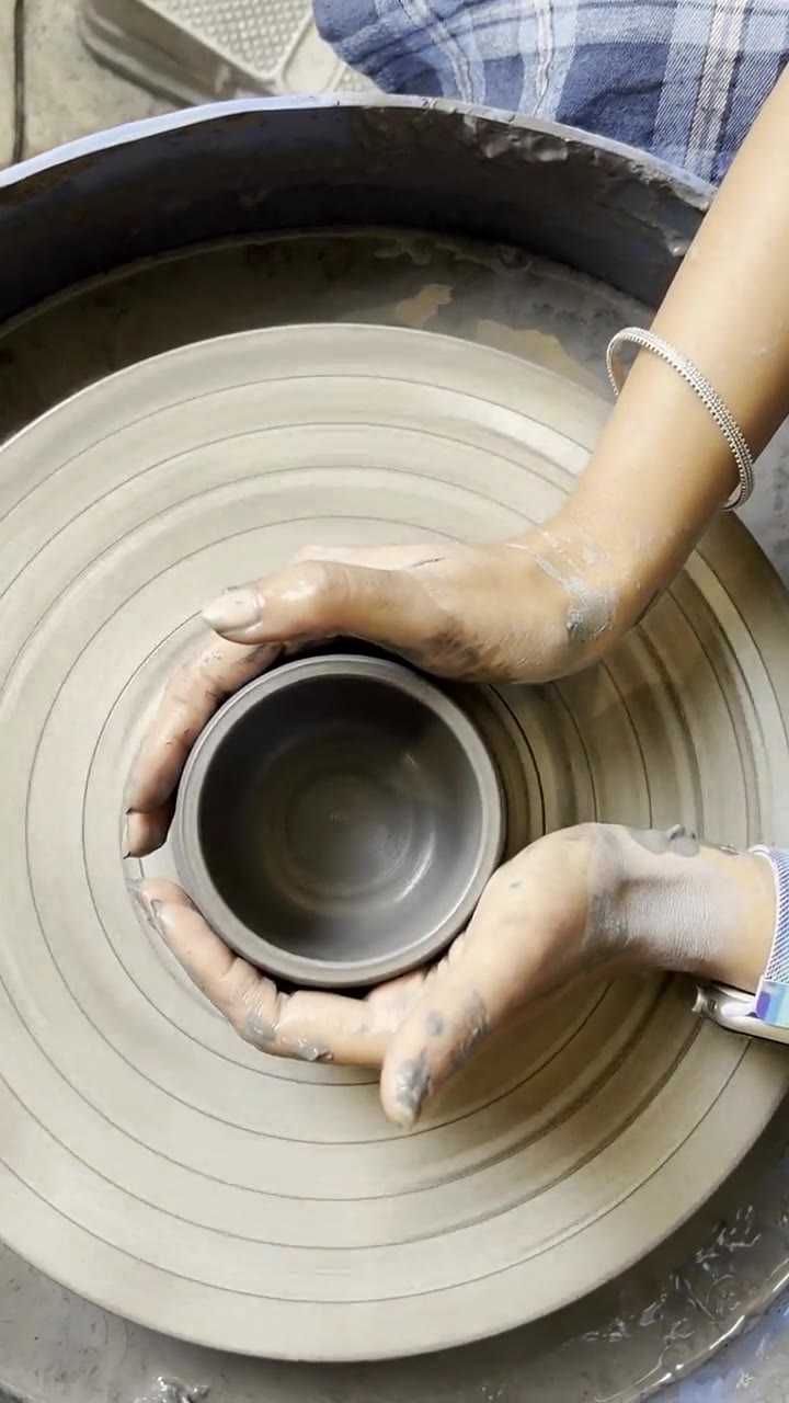 Clay-covered hands closed around a spinning form on the wheel